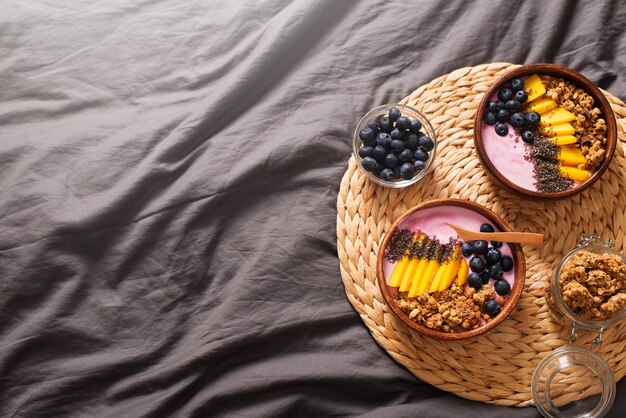 Breakfast on bed with smoothie bowl with granola mango yogurt and blueberry on grey background