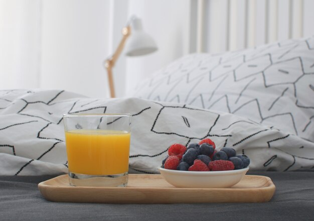 Breakfast bed Wooden tray Early morning  interior Copy space Geometric sheet and pillow case Berries Orange juice Biscuits