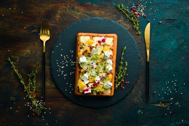 Breakfast. Belgian waffles with brie cheese, feta and parmesan. On a black stone plate.