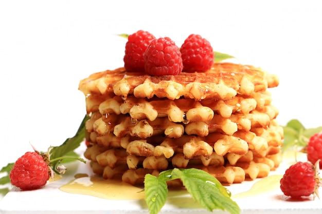 Breakfast belgian waffles with fresh raspberries topped with honey on white wooden