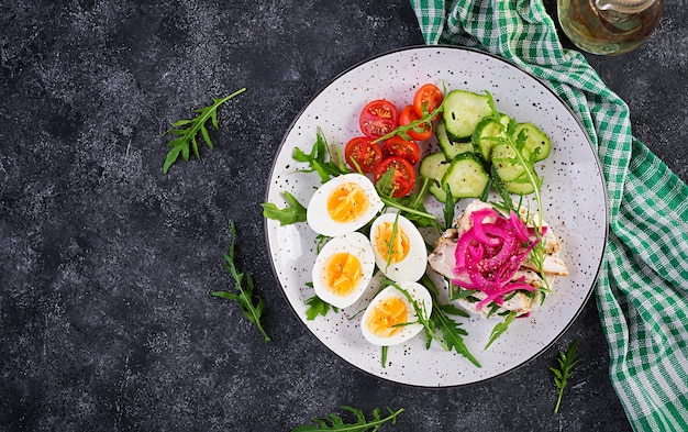 Breakfast. Boiled eggs salad with greens, cucumbers, tomato and sandwich with ricotta cheese, fried chicken fillet and red onion. Keto/paleo lunch. Top view, overhead