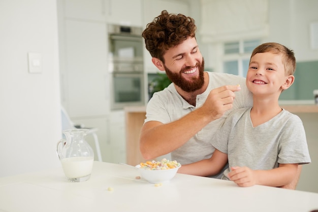 Завтрак приносит первую улыбку дня Снимок очаровательного маленького мальчика и его отца, завтракающих вместе дома