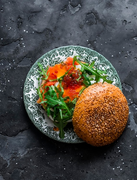 Breakfast burger with egg salmon arugula and red caviar on a dark background top view