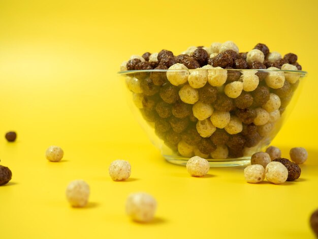 Breakfast cereal Vanilla and chocolate corn balls in a glass bowl on a yellow background