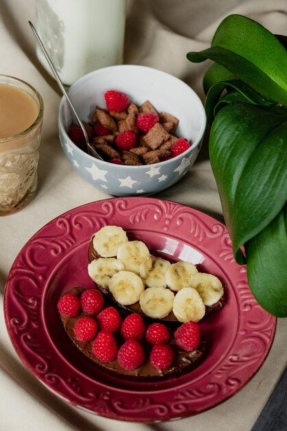 Breakfast, cereal with milk, coffee with milk in a faceted glass, beterbrots with chocolate butter, berries and bananas