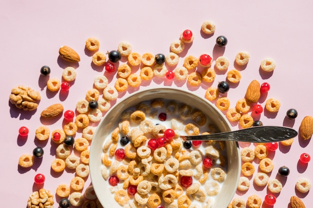 Foto anelli di cereali per la colazione in una ciotola bianca. farina d'avena, fiocchi di mais su una parete rosa. colazione a buffet in hotel o ristorante. anelli di cereali integrali con frutti di bosco. gustoso e salutare