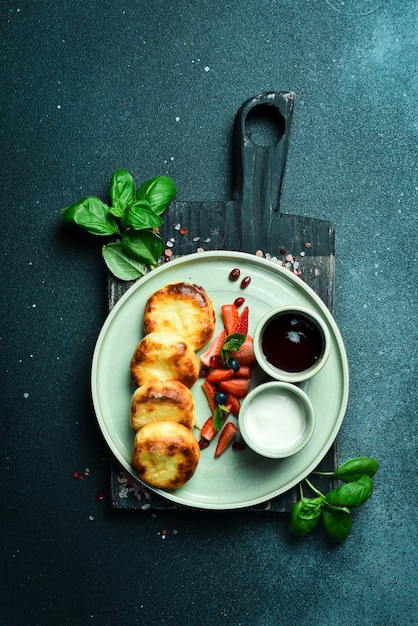 Breakfast Cheese pancakes with sour cream and fruit on a plate On a black stone background