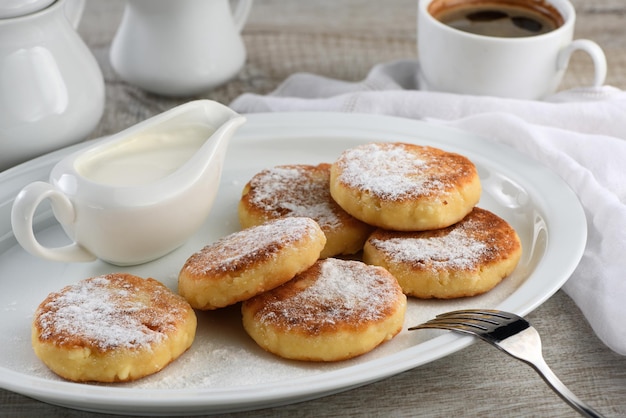 Breakfast. Cheese pancakes with sour cream sprinkled with powdered sugar on a white plate.