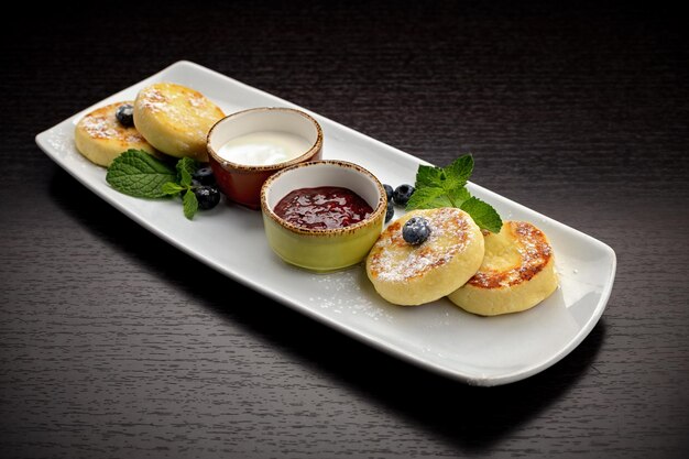 Breakfast cheesecakes with two sauces mint and blueberries on a dark background