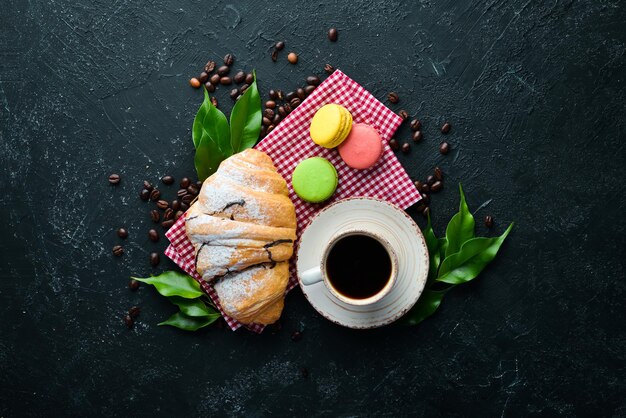 Breakfast Coffee croissant and macaroons On a black stone background Top view Free space for your text