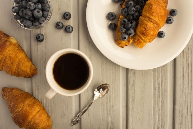 Breakfast: coffee, croissant with peanut paste and blueberries  on the  grey wooden background.Top view.Copy space.