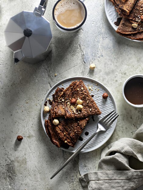 Photo breakfast concept chocolate crepes with nuts and chocolate sauce on a textured background top view