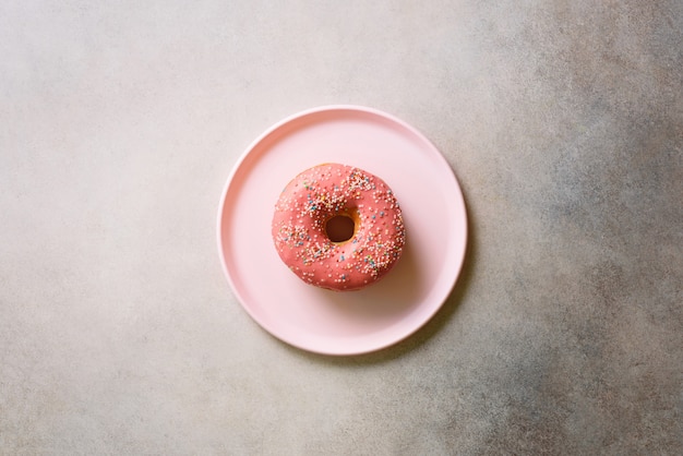 Breakfast concept. Donut on pink plate over concrete background with copy space. 