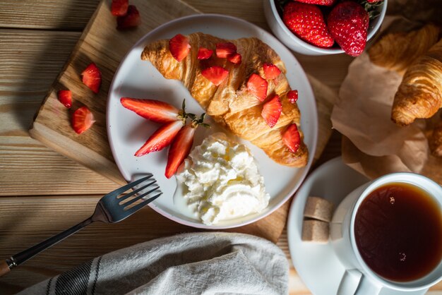 Breakfast concept with coffee cup, croissants, cream and fresh berries.