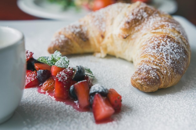 Breakfast dessert - pcroissant with powdered sugar, fruit and sauce, close up, close up view
