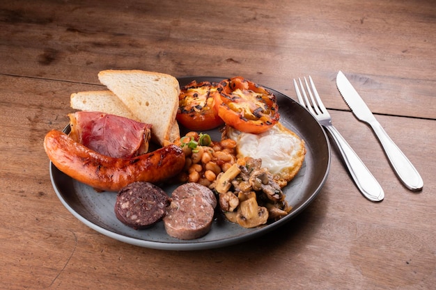 Photo breakfast dish english irish uk with lots of protein sweet beans sausage bacon egg mushrooms black white pudding cutlery