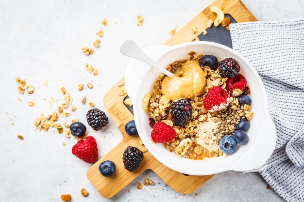 Breakfast food background. Granola with hemp seeds, maca powder, peanut butter and berries on white table.