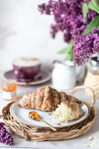 Breakfast French croissant, jam, Cup of coffee, milk and cream and lilac flowers. Morning