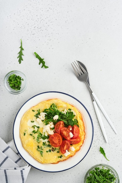 Breakfast fried eggs Rustic omelette or frittatas with green onions cheese mozzarella green arugula and tomatoes on light stone background Healthy food concept Copy space Top view Mock up