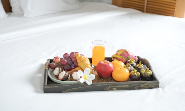 Фото Завтрак, фрукты, круассаны, апельсиновый сок, в черном деревянном подносе, на белой простыне, концепция здорового питания.