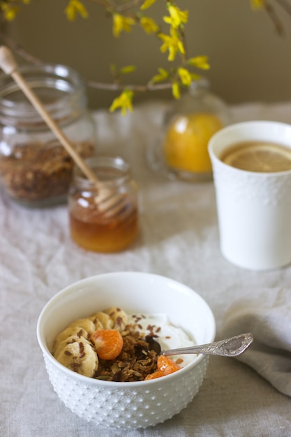 Photo breakfast of granola with yogurt and tea and forsythia flowers on a linen tablecloth. rustic style.