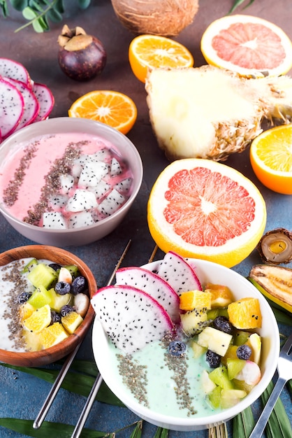 Photo breakfast green yoghurt bowl topped with pitaya, pineapple, chia seeds and berries with palm leaf on stone background, top view