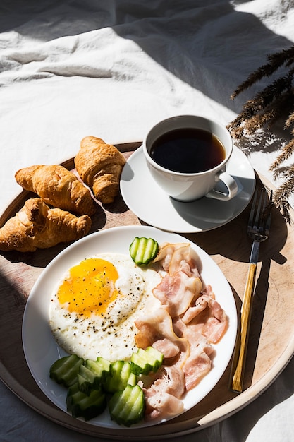 写真 ベッドでの朝食コーヒーカップ目玉焼きベーコンとクロワッサンの木製トレイ