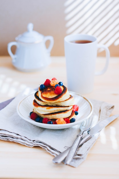 Breakfast, lush pancakes with fresh berries, raspberries and blueberries and a cup of tea