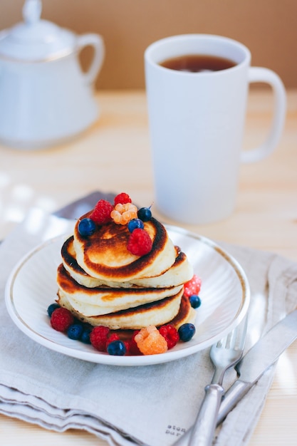 Breakfast, lush pancakes with fresh berries, raspberries and blueberries and a cup of tea