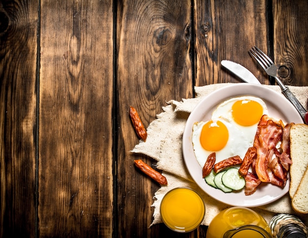 Breakfast in the morning. Fried bacon with eggs and orange juice. On a wooden table.