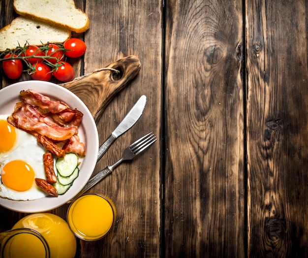 Breakfast in the morning. Fried bacon with eggs and orange juice. On a wooden table.