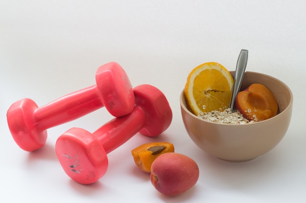 Breakfast oatmeal and fruits near dumbbells