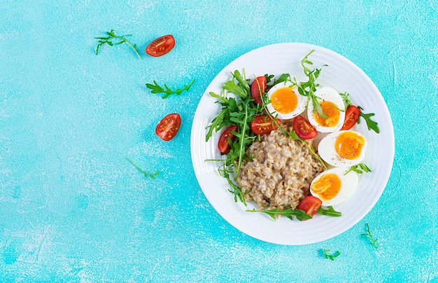 Breakfast oatmeal porridge with boiled egg, cherry tomatoes and arugula