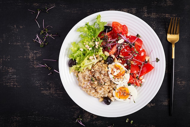 Breakfast oatmeal porridge with boiled egg cherry tomatoes olives nuts and microgreens Healthy balanced food Top view overhead