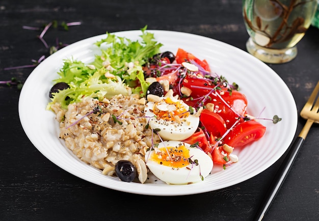 Breakfast oatmeal porridge with boiled egg cherry tomatoes olives nuts and microgreens Healthy balanced food