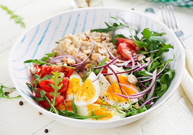 Breakfast oatmeal porridge with boiled eggs tomatoes and red onions Healthy balanced food Trendy food