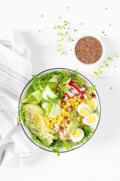 Breakfast oatmeal porridge with fresh vegetable salad of cucumber radish lettuce corn avocado chia seeds and boiled eggs Healthy balanced food Top view Flat lay