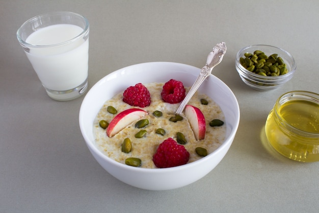 Breakfast: oatmeal with apple,raspberries, honey, nuts and milk in the glass   on the grey  background