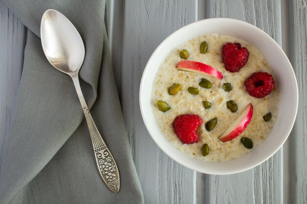 Breakfast: oatmeal with apple,raspberries  and nuts  on the grey wooden  background.Top view.