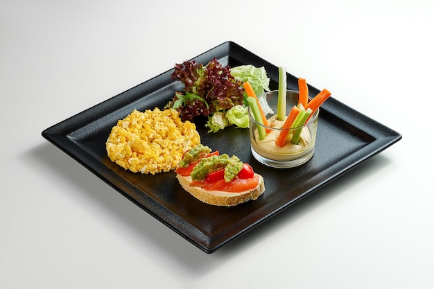 Breakfast omelet with salmon toast and salad in a black plate on a gray background