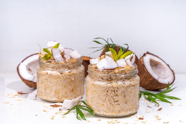 Breakfast overnight oatmeal oats with coconut milk and fresh coconut pieces Diet healthy food vegan diet On light background with fresh coconuts and palm leaves copy space