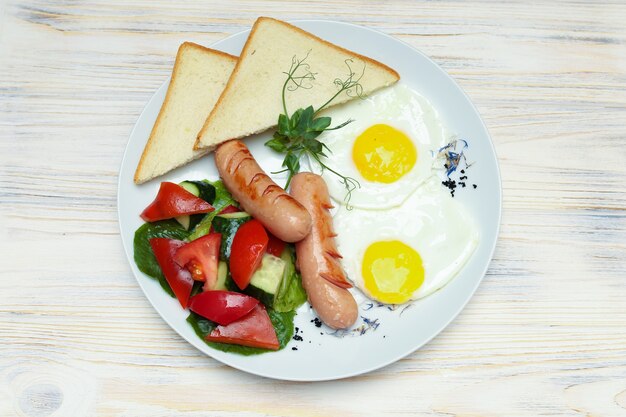 Breakfast plate top view, scrambled eggs with toast and sausages on white plate.