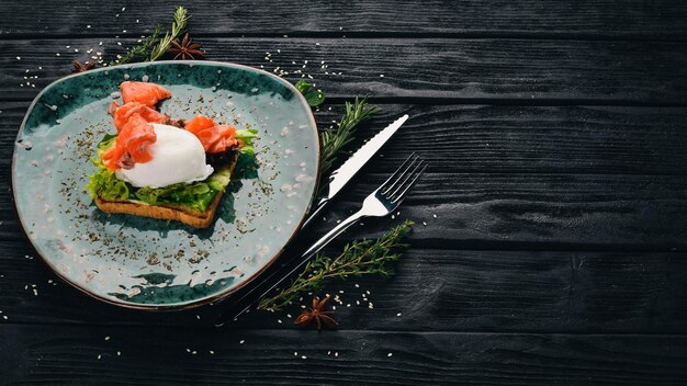 Завтрак. Яйцо пашот, лосось на листьях салата на тостах. На черном деревянном фоне. Скопируйте пространство.