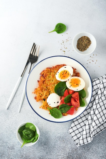 Breakfast Potatoes latkes with sour cream spinach salad tomatoes and boiled eggs on light background Delicious food for breakfast Top view