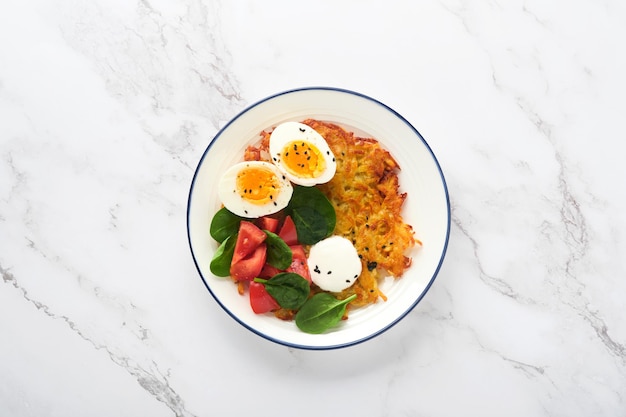 Breakfast potatoes latkes with sour cream spinach salad
tomatoes and boiled eggs on light marble table background delicious
food for breakfast top view