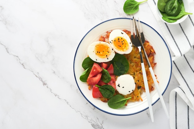 Breakfast Potatoes latkes with sour cream spinach salad tomatoes and boiled eggs on light marble table background Delicious food for breakfast Top view