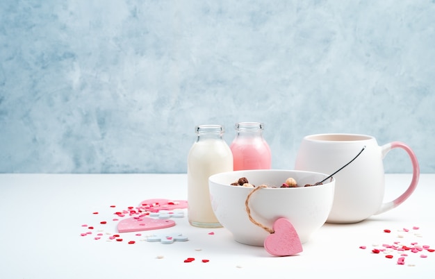 Prima colazione su uno sfondo romantico. cereali in una tazza bianca, caffè con latte e cuori su un blu e