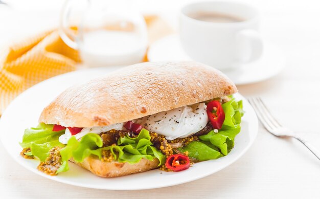 Breakfast in a rustic style on a white wooden surface. ciabatta with poached egg and grain mustard with a hot cup of coffee and fresh