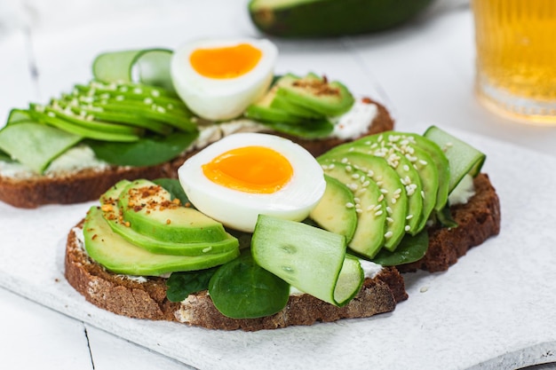 A breakfast sandwich with avocado, avocado, and egg on top.