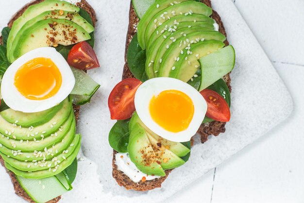 A breakfast sandwich with avocado, avocado, and tomato on top.